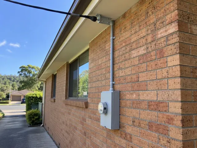 Overhead service cable and point-of-attachment bracket on a brick home exterior in Erina